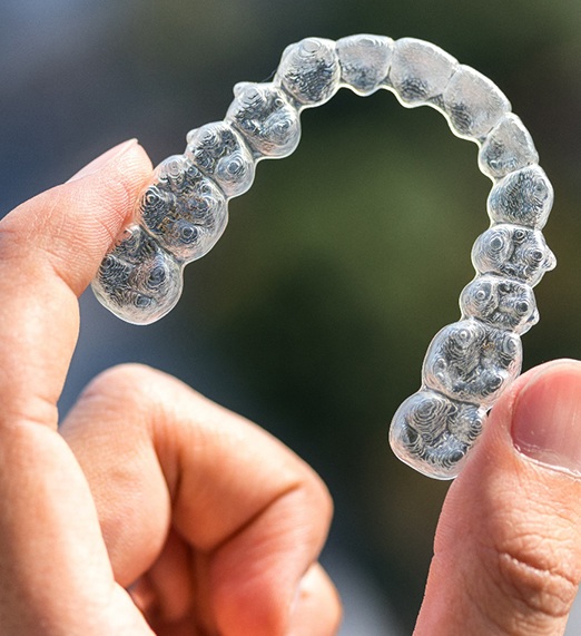 a person holding a clear aligner for Invisalign in Plano